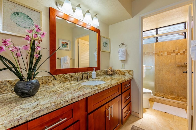 bathroom featuring vanity, toilet, tiled shower, and tile patterned flooring