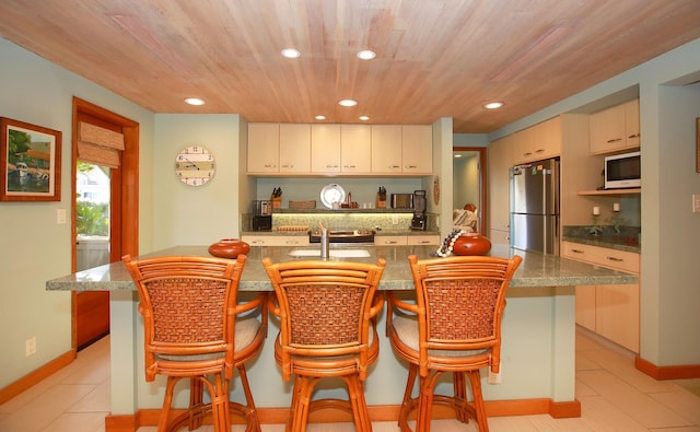 kitchen featuring stainless steel refrigerator, light tile flooring, white microwave, wood ceiling, and a kitchen breakfast bar