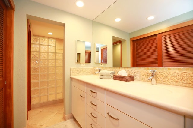 bathroom with tasteful backsplash, vanity with extensive cabinet space, and tile flooring