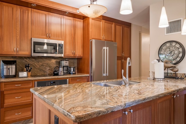 kitchen featuring light stone counters, an island with sink, hanging light fixtures, stainless steel appliances, and backsplash