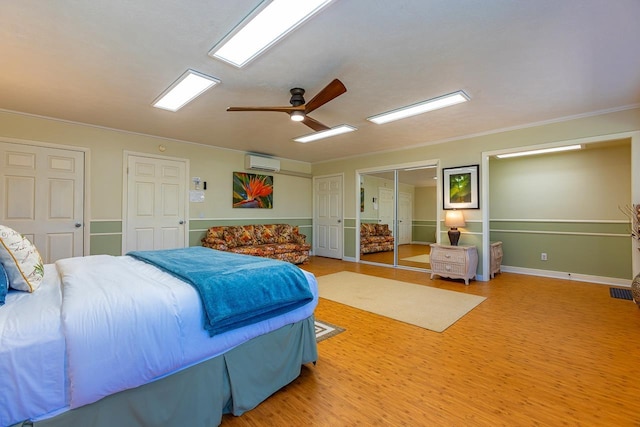 bedroom with two closets, crown molding, ceiling fan, a wall mounted AC, and wood-type flooring