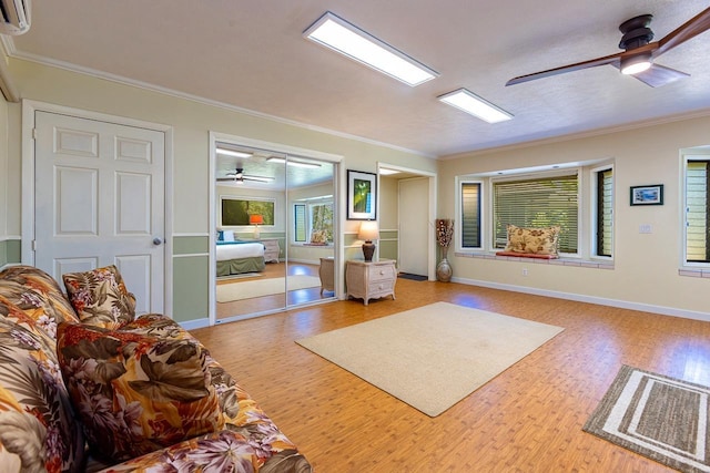 living room featuring wood-type flooring, a wall unit AC, ceiling fan, and crown molding