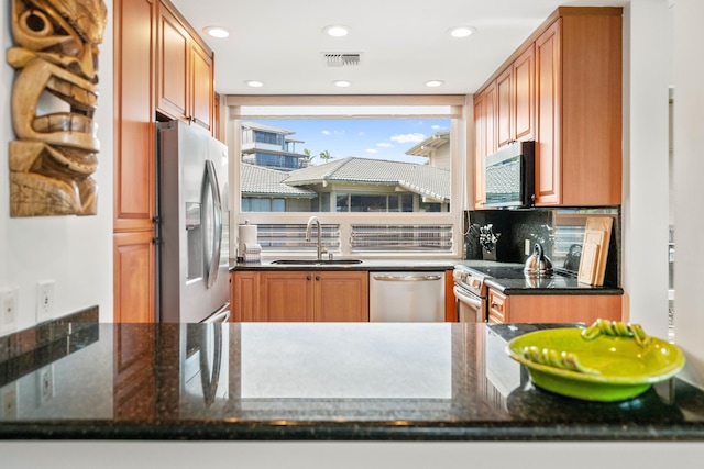 kitchen featuring stainless steel appliances, tasteful backsplash, dark stone counters, and sink