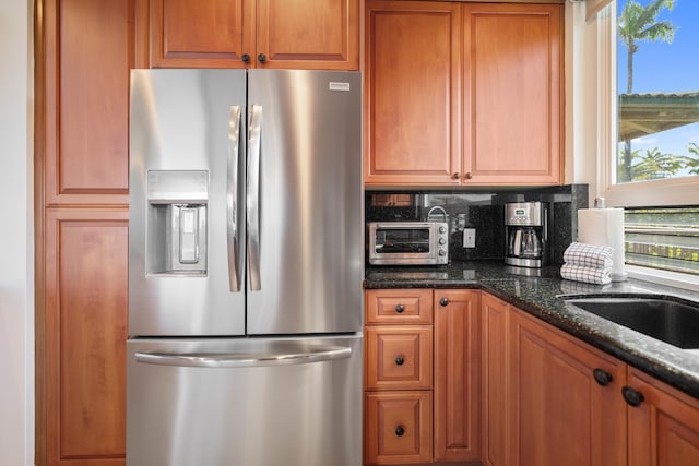 kitchen with backsplash, stainless steel fridge, sink, and dark stone counters