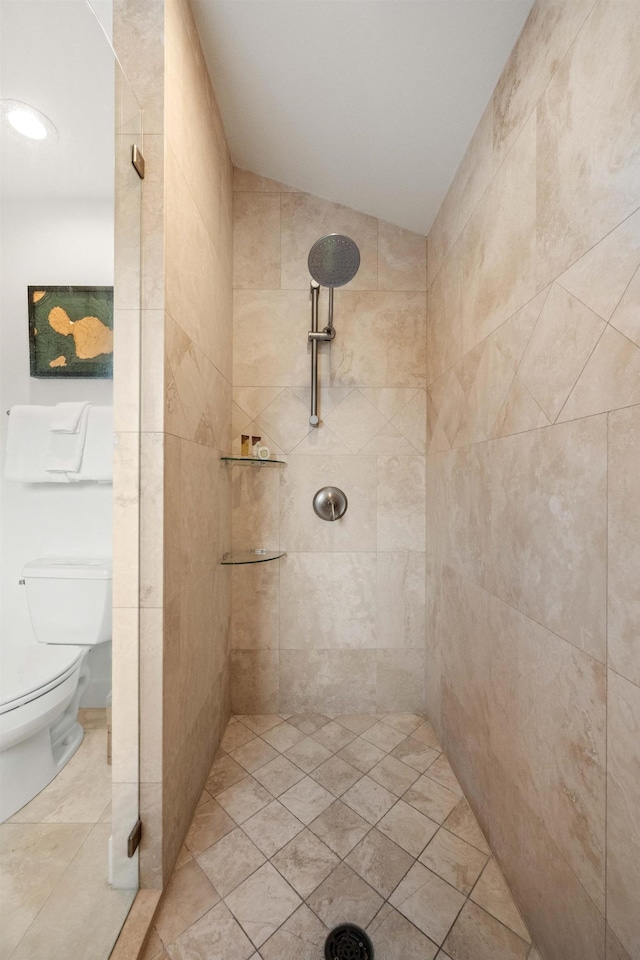 bathroom with tiled shower, tile patterned flooring, vaulted ceiling, and toilet