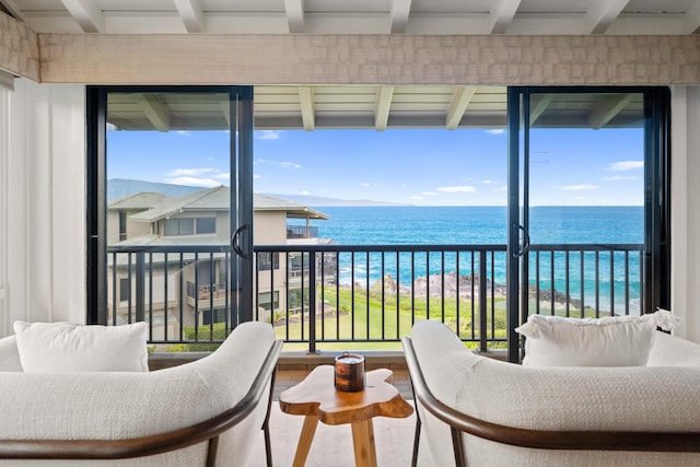 sunroom / solarium featuring beam ceiling, a water view, and a view of the beach