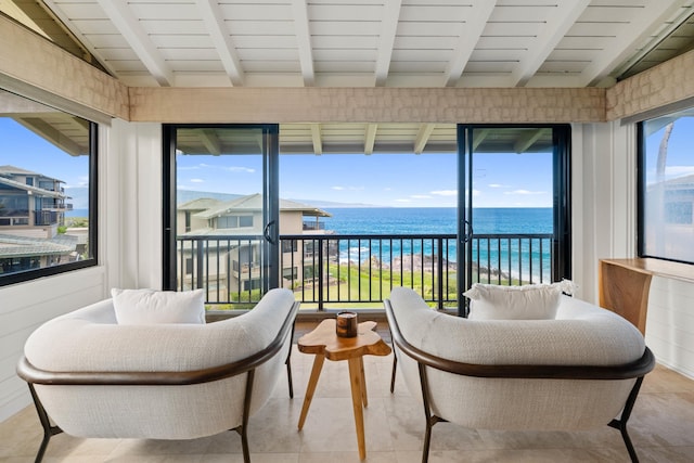 sunroom featuring plenty of natural light, beam ceiling, a water view, and a beach view