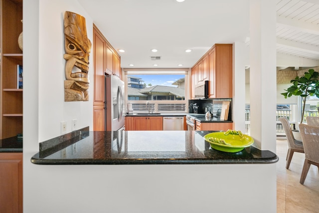 kitchen with kitchen peninsula, sink, dark stone countertops, and appliances with stainless steel finishes