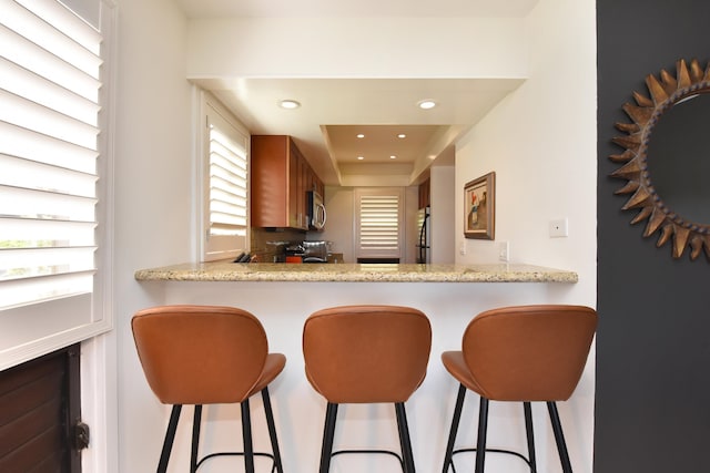 kitchen featuring kitchen peninsula, light stone countertops, stainless steel appliances, and a breakfast bar