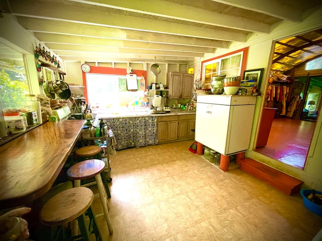 kitchen with beamed ceiling, white refrigerator, and a kitchen bar