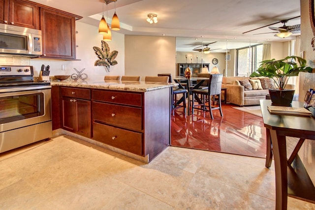 kitchen featuring light hardwood / wood-style flooring, decorative light fixtures, light stone counters, kitchen peninsula, and stainless steel appliances