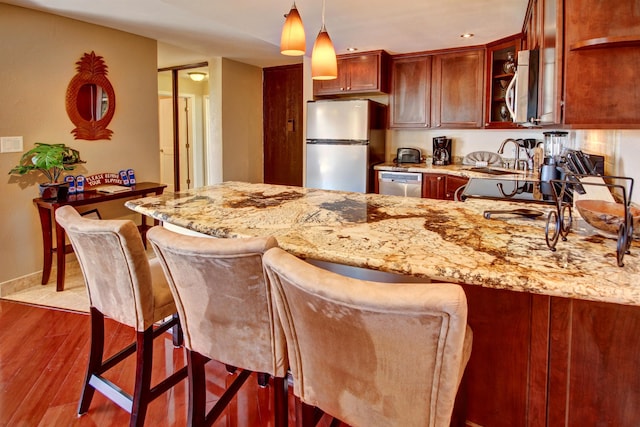 kitchen featuring light hardwood / wood-style flooring, appliances with stainless steel finishes, decorative light fixtures, light stone counters, and kitchen peninsula