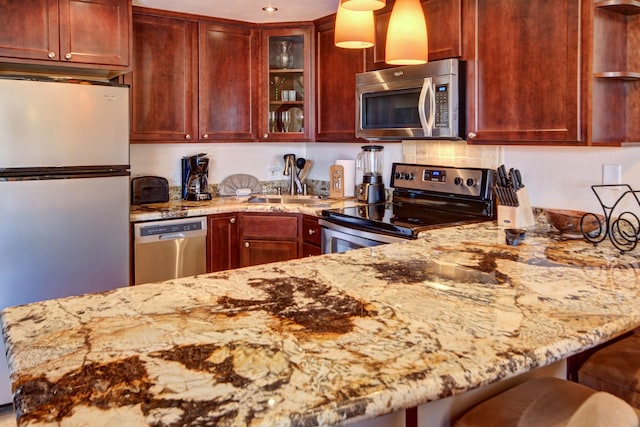 kitchen with kitchen peninsula, appliances with stainless steel finishes, light stone countertops, sink, and a breakfast bar area