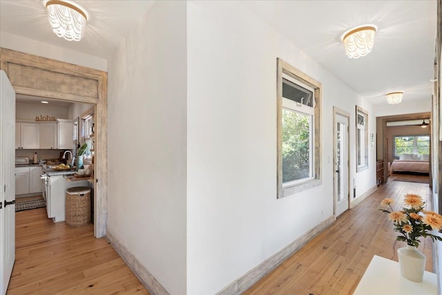 corridor with baseboards, a sink, and light wood finished floors