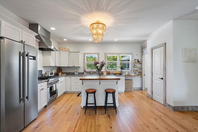 kitchen with wall chimney range hood, high end appliances, light wood-type flooring, and white cabinetry