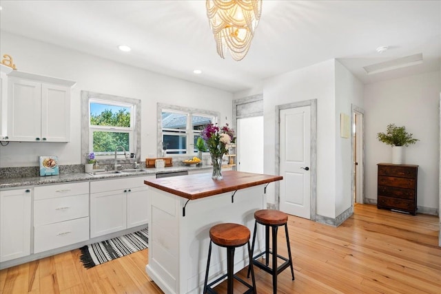 kitchen with light wood finished floors, white cabinets, wood counters, a sink, and recessed lighting