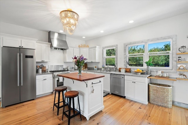 kitchen featuring stainless steel appliances, white cabinets, wall chimney range hood, and wood counters