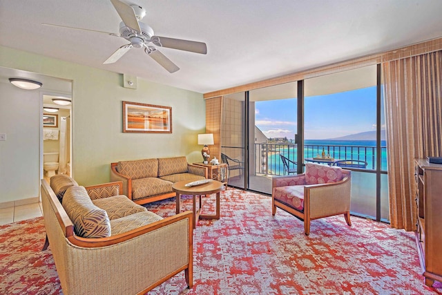 living room with ceiling fan, a water view, and a wall of windows