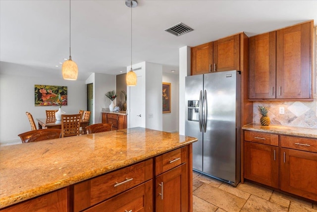 kitchen with light stone counters, stainless steel refrigerator with ice dispenser, hanging light fixtures, and tasteful backsplash