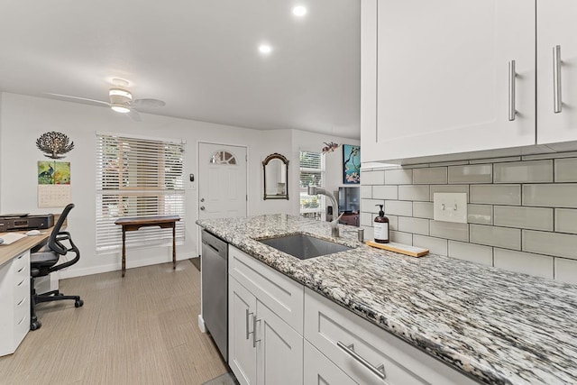 kitchen with light stone countertops, stainless steel dishwasher, sink, and white cabinets