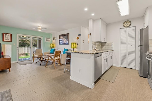 kitchen with appliances with stainless steel finishes, kitchen peninsula, light stone countertops, and white cabinets