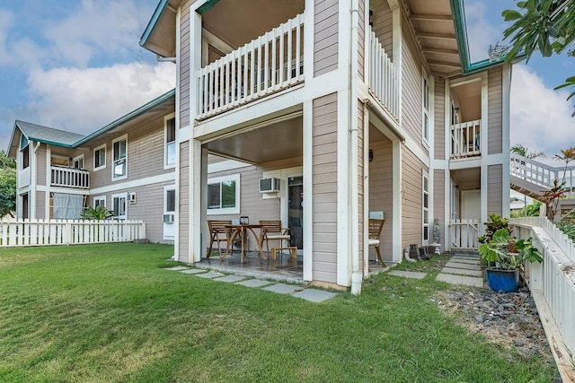 rear view of house featuring a balcony, a wall unit AC, a patio area, and a lawn