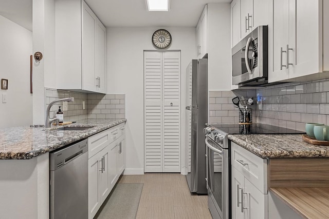 kitchen featuring stainless steel appliances, white cabinetry, stone counters, and backsplash