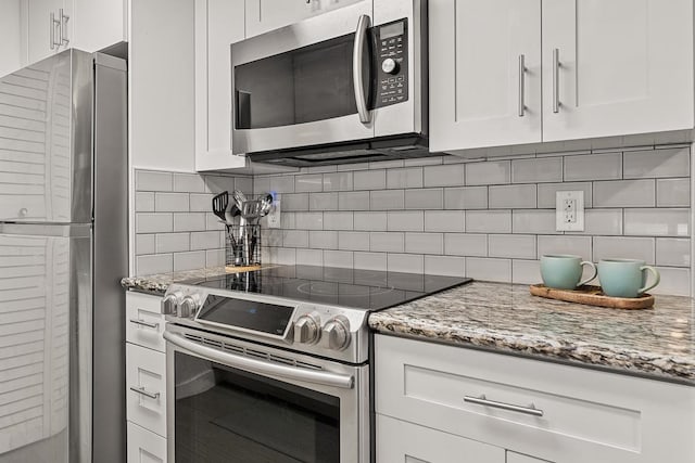 kitchen with light stone countertops, stainless steel appliances, white cabinets, and backsplash