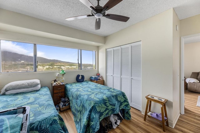 bedroom with a textured ceiling, a closet, a mountain view, light wood-type flooring, and ceiling fan