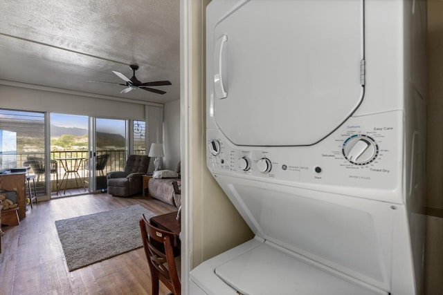 washroom with ceiling fan, wood-type flooring, stacked washer / drying machine, and a textured ceiling