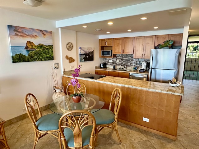 kitchen featuring light stone countertops, kitchen peninsula, tasteful backsplash, stainless steel appliances, and sink