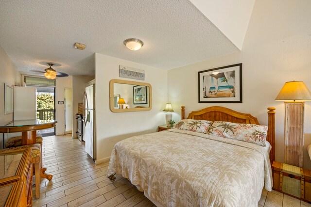 bedroom with ceiling fan, a textured ceiling, white fridge, and light wood-type flooring