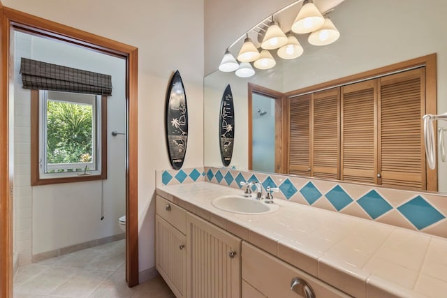 bathroom featuring tasteful backsplash, toilet, tile patterned flooring, vanity, and baseboards