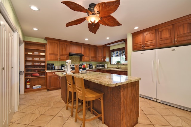 kitchen featuring freestanding refrigerator, a sink, ceiling fan, stainless steel microwave, and a center island