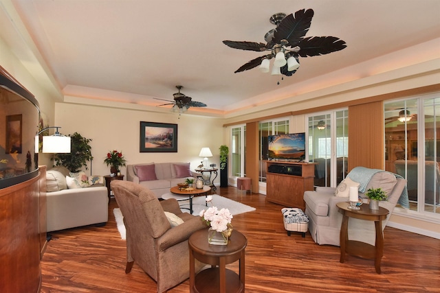 living room with a ceiling fan, a tray ceiling, and wood finished floors