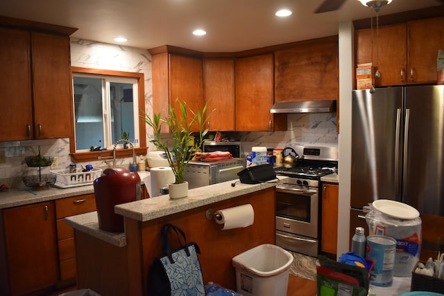 kitchen featuring tasteful backsplash, under cabinet range hood, recessed lighting, brown cabinetry, and stainless steel appliances