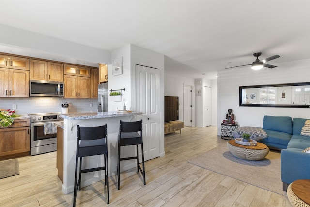 kitchen with brown cabinets, a breakfast bar area, stainless steel appliances, light wood-style floors, and open floor plan