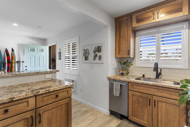 kitchen featuring tasteful backsplash, stainless steel dishwasher, light wood-style floors, brown cabinetry, and a sink