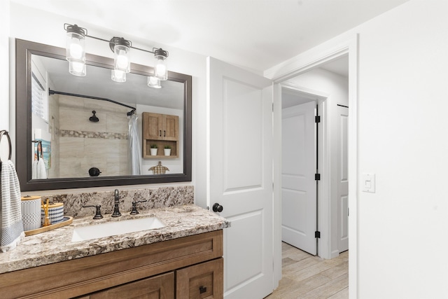 full bathroom featuring tiled shower, vanity, and wood finished floors