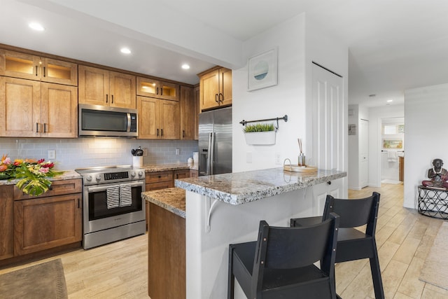 kitchen featuring decorative backsplash, brown cabinets, a breakfast bar, a peninsula, and stainless steel appliances