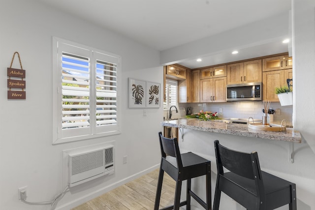 kitchen with a wall unit AC, light wood finished floors, stainless steel microwave, a kitchen bar, and tasteful backsplash