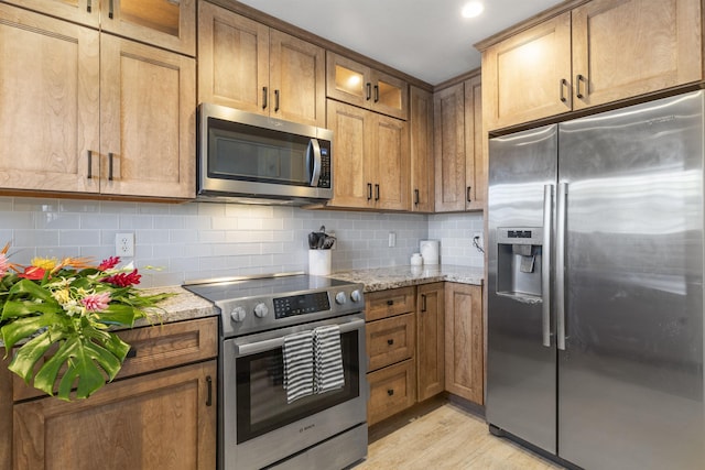 kitchen featuring light wood-style floors, tasteful backsplash, light stone counters, and stainless steel appliances