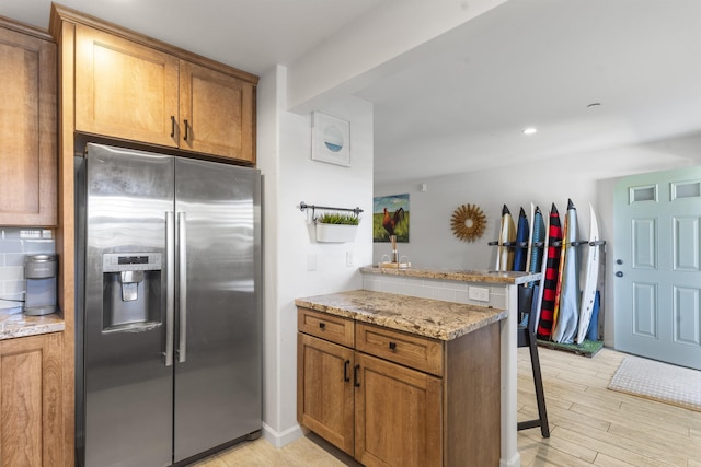 kitchen with a peninsula, brown cabinetry, stainless steel fridge, and a kitchen breakfast bar