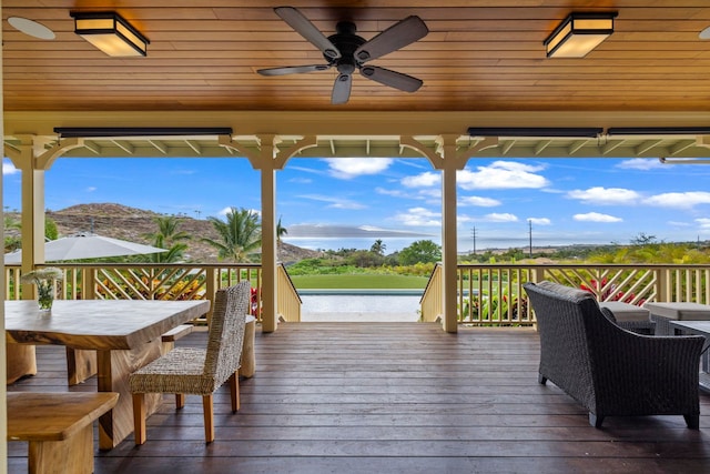 wooden terrace featuring outdoor dining area, a ceiling fan, and a water view