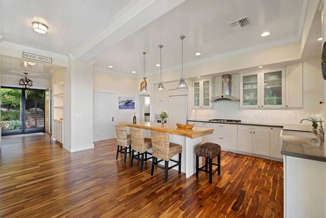 kitchen with wall chimney range hood, white cabinetry, ornamental molding, dark hardwood / wood-style floors, and paneled built in fridge