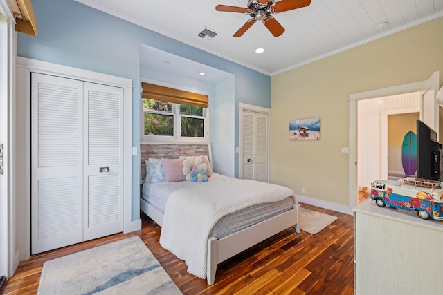 bedroom with dark hardwood / wood-style flooring, ornamental molding, two closets, and ceiling fan