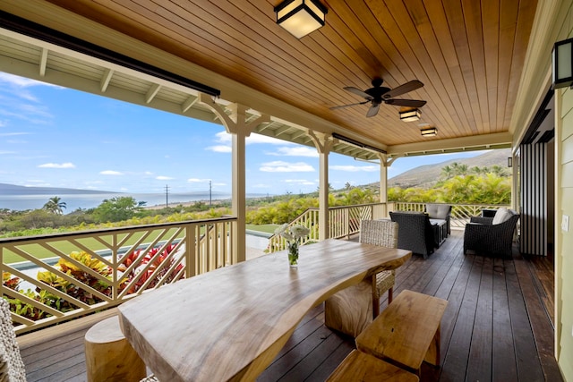 wooden terrace with a mountain view, outdoor dining space, and ceiling fan