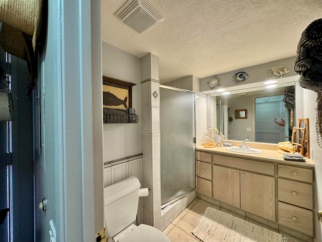 bathroom featuring a shower with door, vanity, a textured ceiling, tile patterned flooring, and toilet