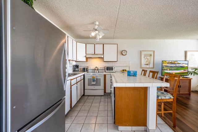 kitchen featuring stainless steel refrigerator, electric range, tile counters, white cabinets, and a textured ceiling