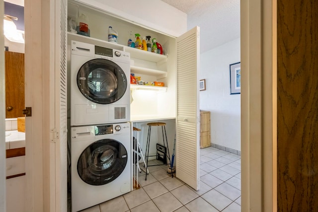 laundry area featuring stacked washing maching and dryer, light tile patterned floors, and a textured ceiling